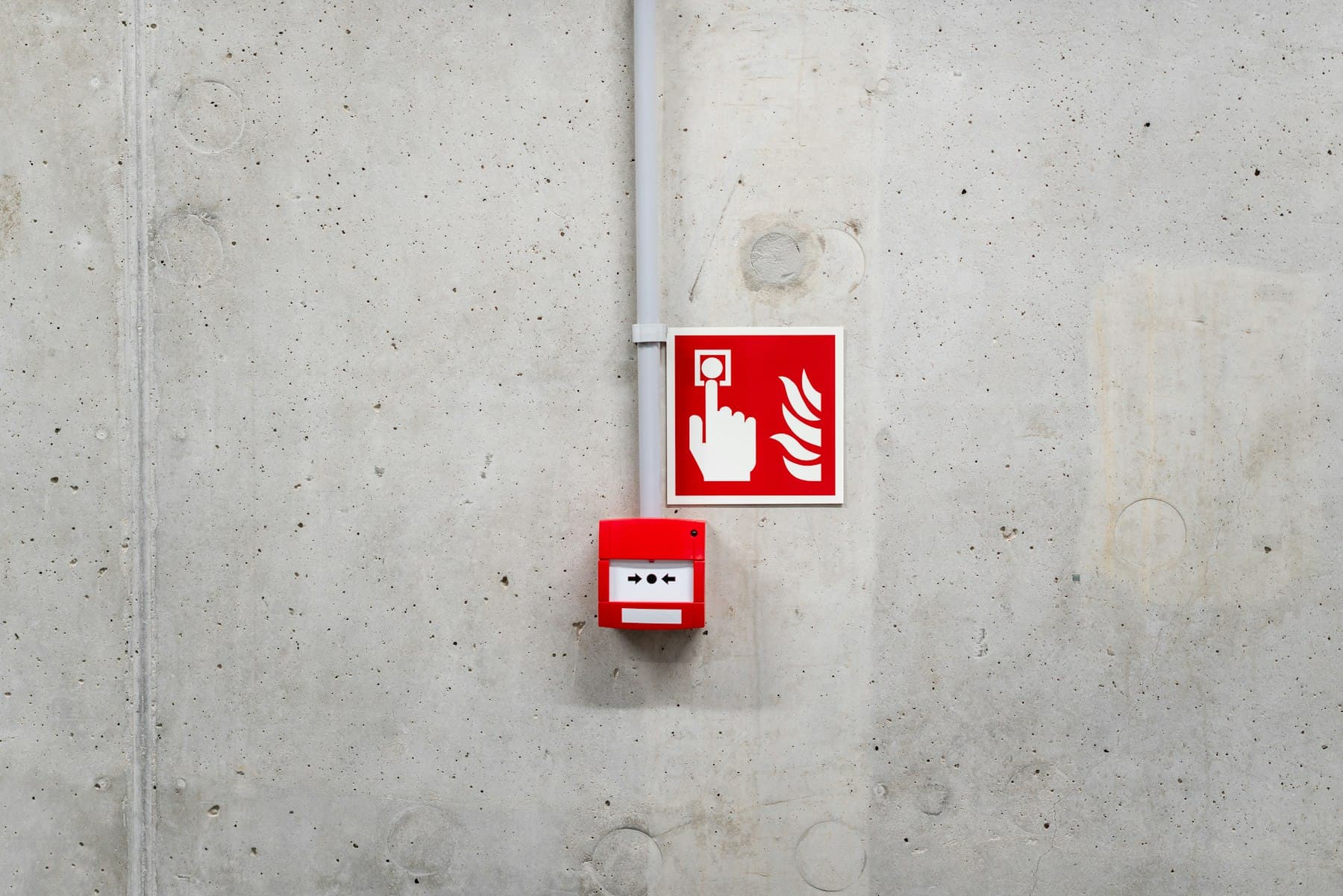 Red manual call point with a fire alarm sign mounted on a concrete wall