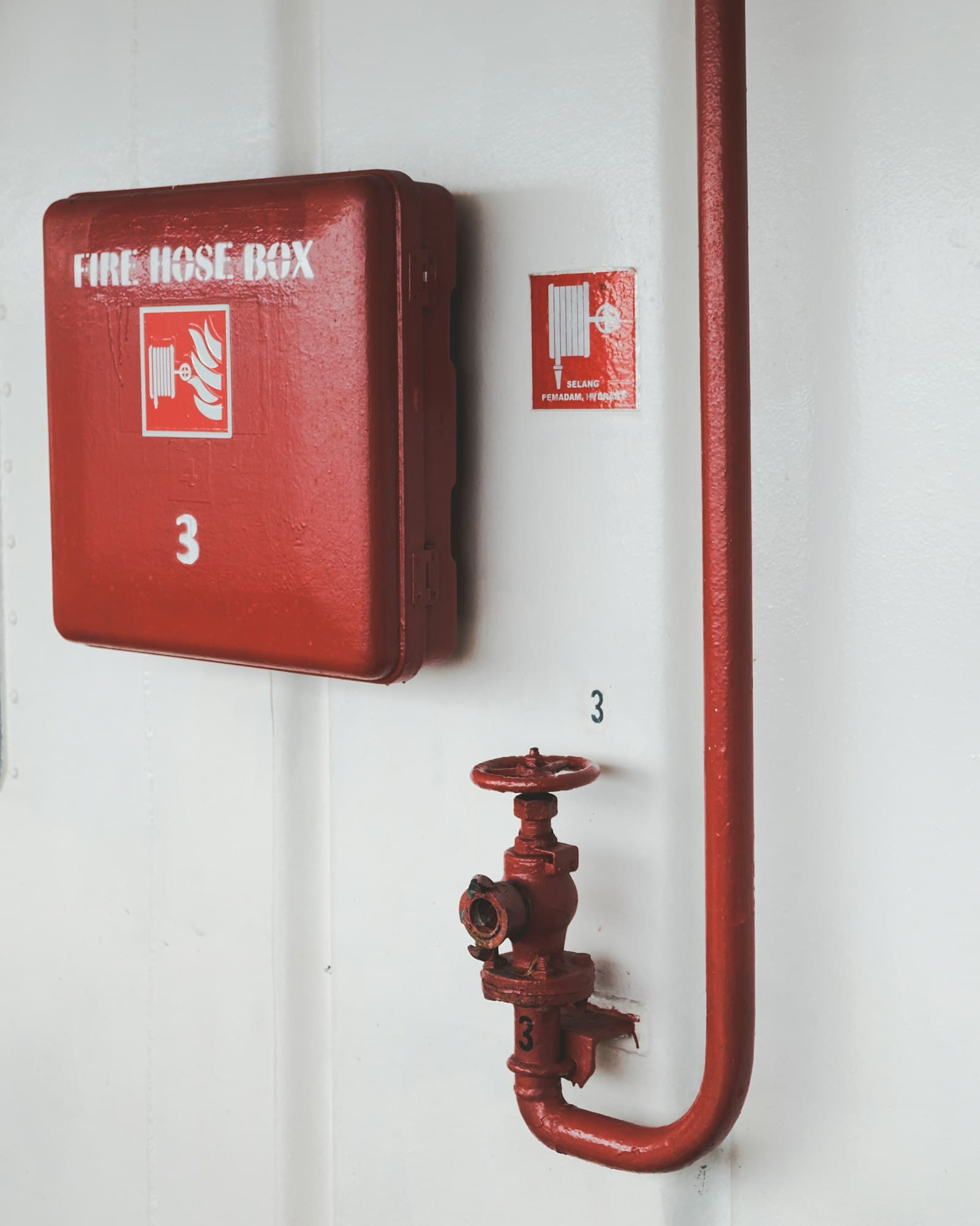 Red fire hose box and hydrant valve mounted on a white wall