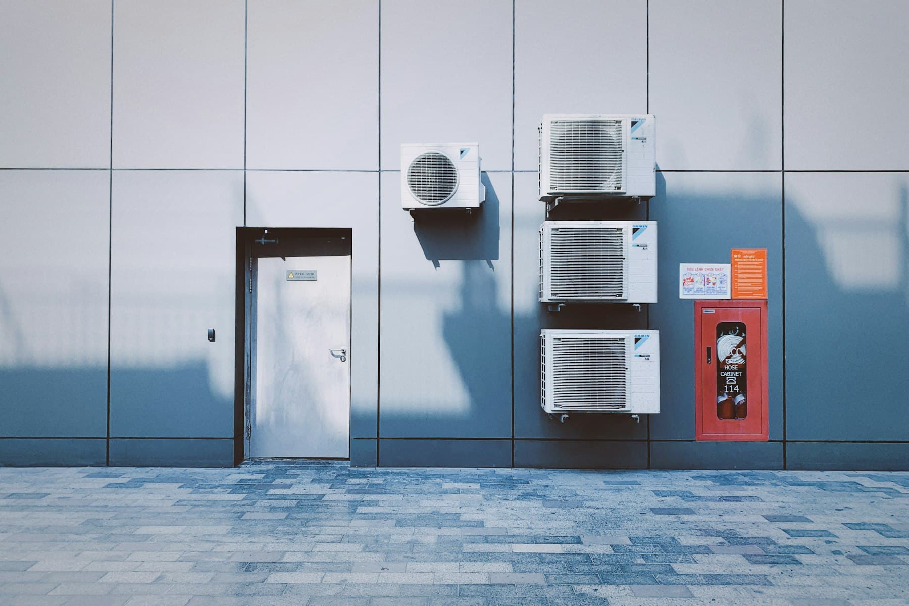 Wall-mounted air conditioning units beside a fire hose cabinet on a commercial building